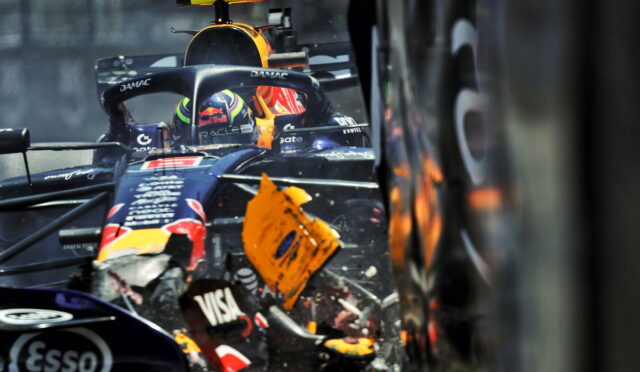 Close-up of a Red Bull Formula 1 car in a crash, with a damaged front wing and debris flying near the cockpit.