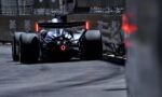 Rear view of a Formula 1 race car racing along a street circuit, red taillights glowing, barriers on both sides.