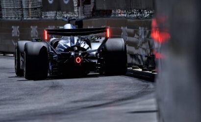 Rear view of a Formula 1 race car racing along a street circuit, red taillights glowing, barriers on both sides.
