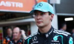 Male Formula 1 driver wearing a turquoise Mercedes cap and Petronas racing suit in the pit area.