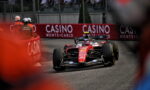 Red Formula 1 car rounds a tight street corner with crowd and Casino barriers in the background at Monte Carlo race. Captures high-speed action on a crowded track.