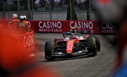 Red Formula 1 car rounds a tight street corner with crowd and Casino barriers in the background at Monte Carlo race. Captures high-speed action on a crowded track.