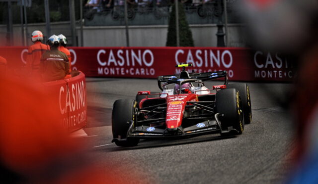 Red Formula 1 car rounds a tight street corner with crowd and Casino barriers in the background at Monte Carlo race. Captures high-speed action on a crowded track.