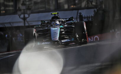 Mercedes-AMG F1 car racing on a track, front view with prominent Petronas branding and blue-green livery, action-packed moment on the straightaway