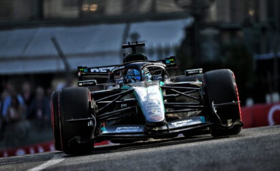 Front view of a Mercedes Formula 1 car speeding along a race track, teal-silver livery and sponsor logos visible on the body.