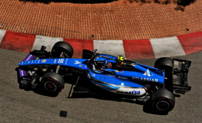 Blue Formula 1 car racing along a track with red and white curb, sponsor logos visible on the blue chassis (Atlassian).] ,