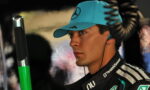 Side profile of a race driver wearing a teal cap and TeamViewer racing suit, listening with an in-ear headset in a pit area