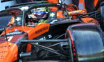 Orange Formula 1 car cockpit with driver wearing helmet, branding visible (Richard Mille, allwyn) and sponsor logos on the nose and halo bar.