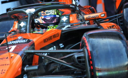 Orange Formula 1 car cockpit with driver wearing helmet, branding visible (Richard Mille, allwyn) and sponsor logos on the nose and halo bar.