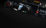 Mercedes F1 race car speeding on track near barriers with AWS branding in the background.