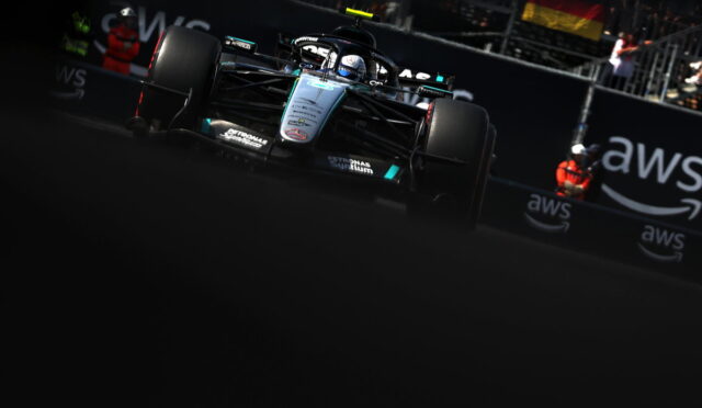 Mercedes F1 race car speeding on track near barriers with AWS branding in the background.