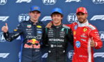 Three Formula 1 drivers pose on a podium in racing suits (Red Bull, Mercedes Petronas, Ferrari) with thumbs up in front of FIA backdrop.