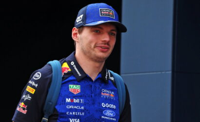 Portrait of a young man in Oracle Red Bull Racing blue cap and polo, with a blue backpack, looking off to the side.