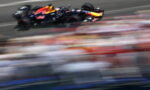 Red Bull Formula 1 car speeding on a race track with blurred grandstands in the background.