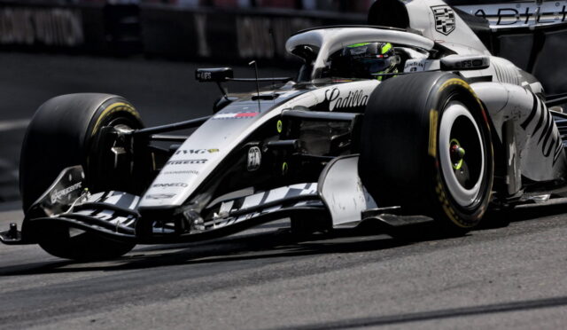 White Formula 1 car corners on a race track, driver in helmet visible inside the cockpit, Cadillac branding on the nose and side.