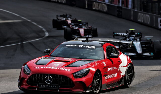 Red Mercedes AMG safety car leading a pack of Formula 1 cars on a race track, sponsor logos visible on the bodywork and hood.