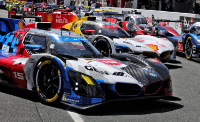 Lineup of colorful race cars in a pit lane, sponsor logos visible on the livery.