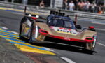 Cadillac race car speeding around a track, blue-yellow curbs visible, crowd in background