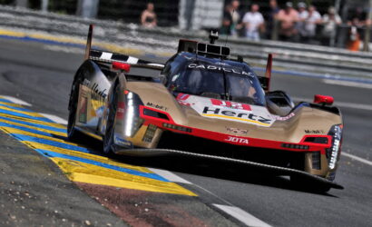 Cadillac race car speeding around a track, blue-yellow curbs visible, crowd in background