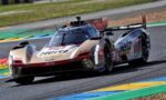 Beige Hertz Cadillac DPi race car navigating a curve on a track with colorful curbs.