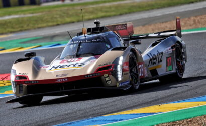 Beige Hertz Cadillac DPi race car navigating a curve on a track with colorful curbs.