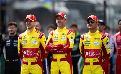 Three yellow-red race drivers stand with arms crossed in a pit lane, matching sponsor logos visible on their suits: Esa NanoTech and Michelin.