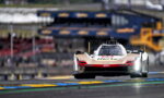 Low-angle front view of a white and red Cadillac race car speeding toward the camera on a race track, with blurred pit area in the background.