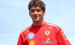 Young man in a red Ferrari shirt with sponsor logos, smiling against a blue sky.