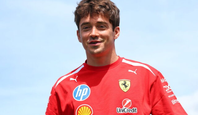 Young man in a red Ferrari shirt with sponsor logos, smiling against a blue sky.