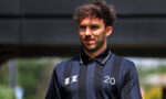 Young man in a navy striped polo with the number 20 on his chest, outdoors under a shaded area.