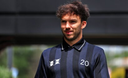 Young man in a navy striped polo with the number 20 on his chest, outdoors under a shaded area.
