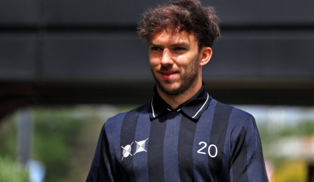 Young man wearing a navy and black striped polo shirt with the number 20, outdoors, looking slightly to the side and smiling.