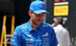 Man in blue polo and cap with Alpine/BWT logos, looking downward in a pit area.