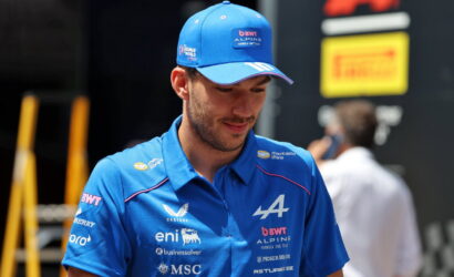 Man in blue polo and cap with Alpine/BWT logos, looking downward in a pit area.