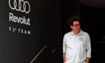 Man in a white Revolut F1 Team polo shirt stands beside a dark wall with the Audi rings logo and 'Revolut' branding.