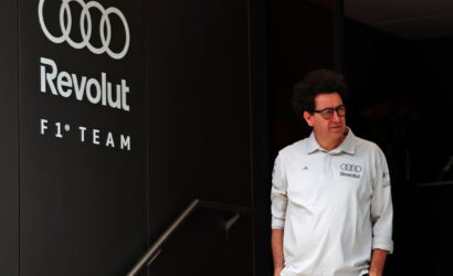 Man in a white Revolut F1 Team polo shirt stands beside a dark wall with the Audi rings logo and 'Revolut' branding.