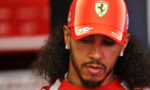 Man in a red Ferrari cap looking down, close-up portrait with earrings and beard.