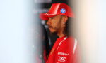 Side profile of a man in a red Ferrari team cap and shirt, facing left in a backstage area.
