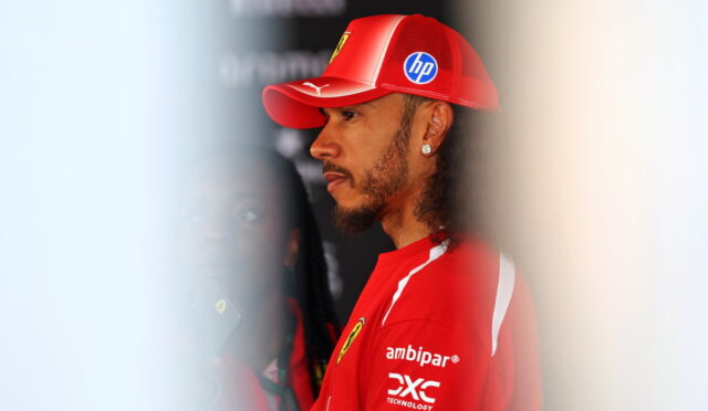 Side profile of a man in a red Ferrari team cap and shirt, facing left in a backstage area.