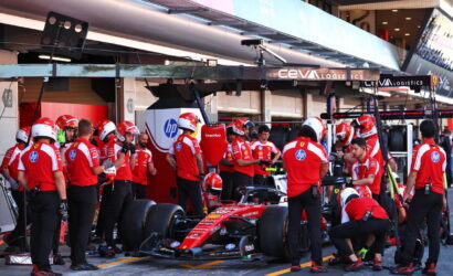Ferrari Formula 1 pit crew in red uniforms working on a red race car in the pit lane, with CEVA Logistics signage overhead.