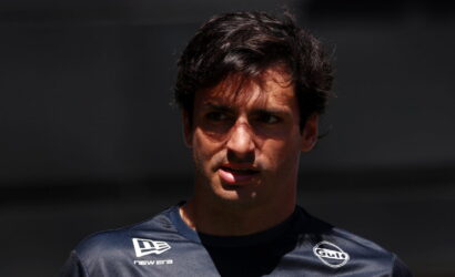 Close-up portrait of a dark-haired man in a navy sponsor jersey, looking off to the left, with Gulf and New Era logos visible on the chest.