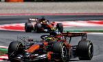Orange and black Formula 1 car leading a race on a curved track with a second car behind it.