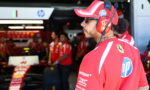 Side profile of a Ferrari pit crew member in a red cap and headset, standing in the pit lane with team members in the background, HP logo visible on the shirt.