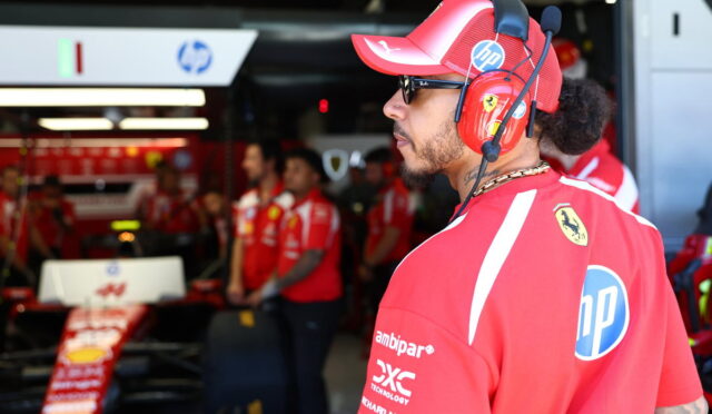 Side profile of a Ferrari pit crew member in a red cap and headset, standing in the pit lane with team members in the background, HP logo visible on the shirt.