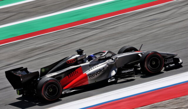 Red and silver Formula 1 car with Revolt branding speeds along a race track with green and red run-off lines in the background.