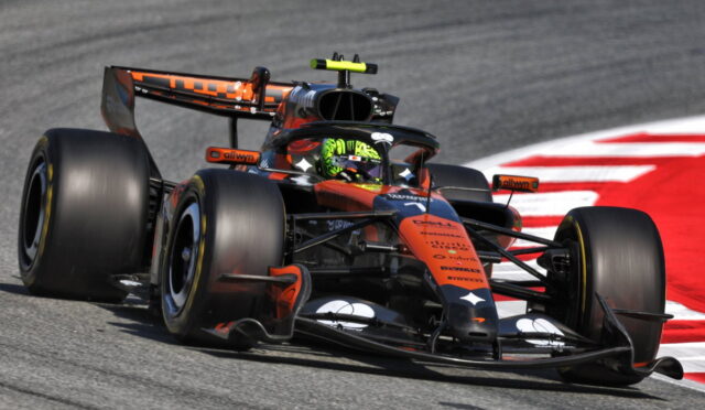 Orange and black Formula 1 race car rounding a left-hand turn on a gray track with a red curb in the background.