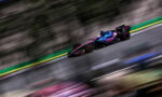 Formula 1 car with pink and blue BWT livery speeding along a race track, motion blur in the background.