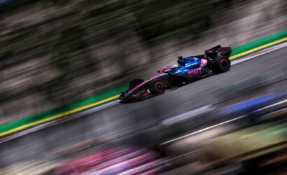 Formula 1 car with pink and blue BWT livery speeding along a race track, motion blur in the background.