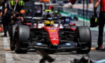 Red Ferrari Formula 1 car on the pit lane ready for a stop, driver in yellow helmet visible.