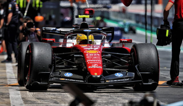 Red Ferrari Formula 1 car on the pit lane ready for a stop, driver in yellow helmet visible.